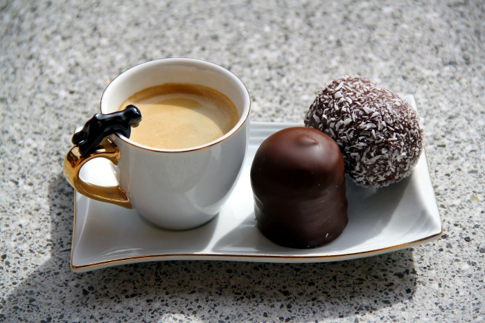 chocolate, coconut ball and cup of coffee on a white platter Coffee with a coconut ball and a chocolate.