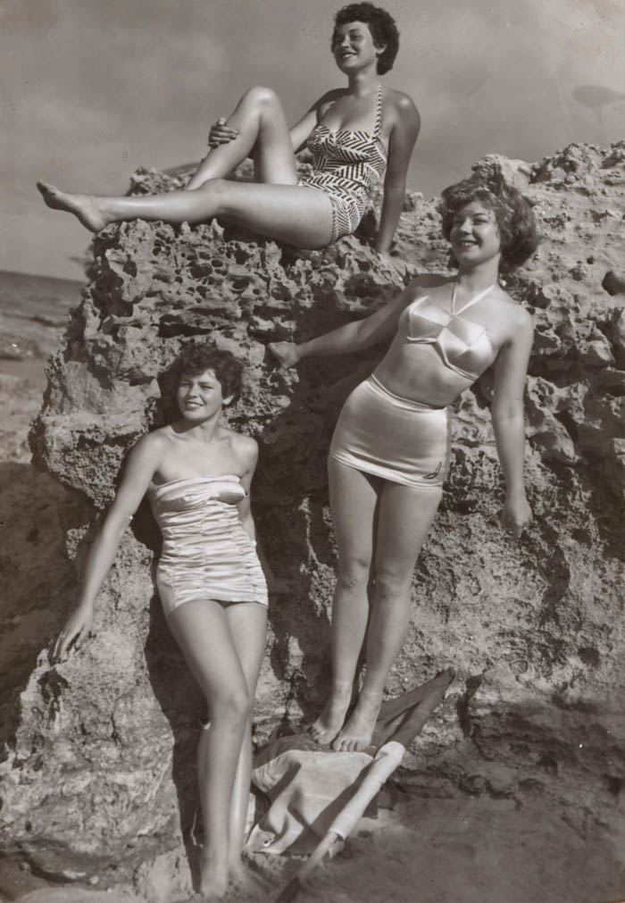 a black and white photo of three women showing the history of swim suits. they are all wearing different bathing suits including one two piece swimsuit. history of the bikini research shows a photo of the earliest two-piece swimsuits