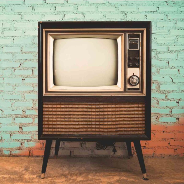An early color TV set which is turned off in front of a teal brick wall.