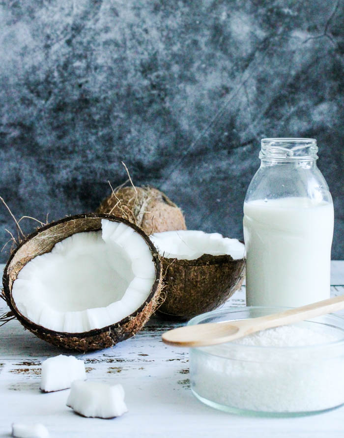 a bottle containing cream of coconut, coconut cream, or coconut milk sits on a table next to a raw coconut and coconut sugar. a bottle of Coconut milk, coconut cream or cream of coconut