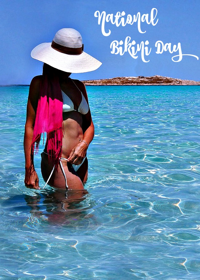 girl in a bikini with a white hat standing in the ocean with the text reading "national bikini day." Girl standing in the water in a bikini for National Bikini Day