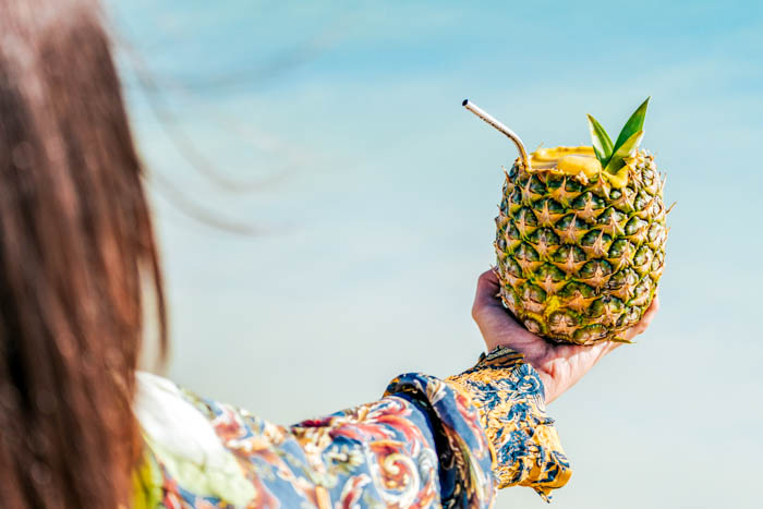 woman holding a pina colada in a pineapple at the beach