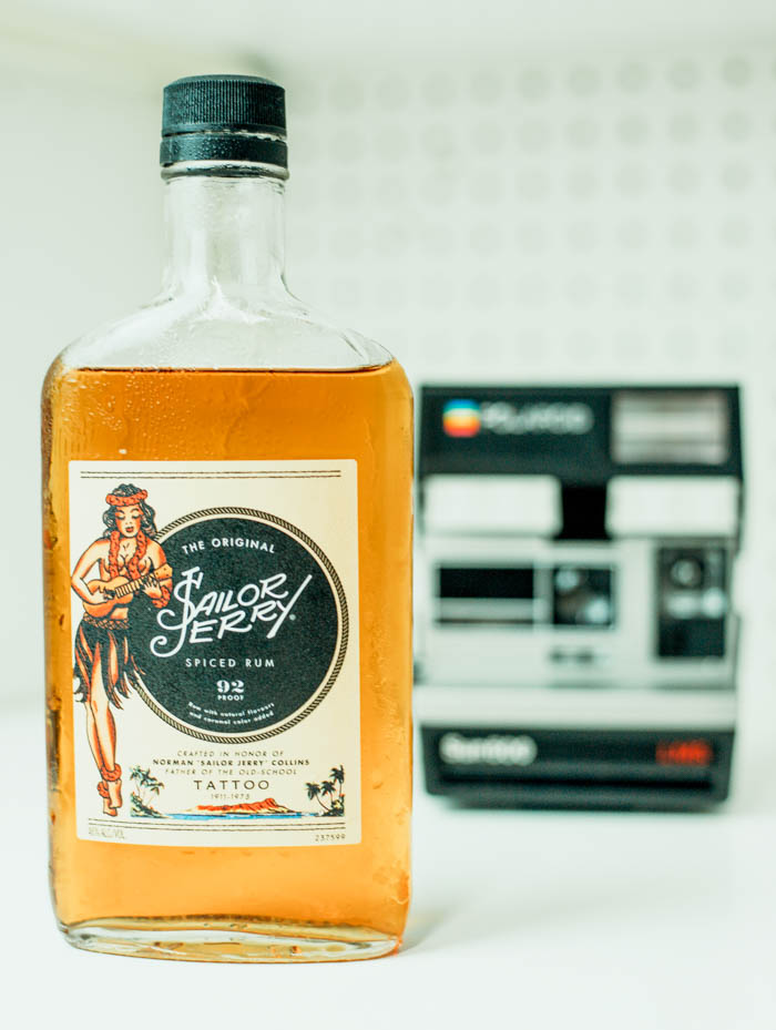 a bottle of sailor jerry which is a spiced rum used in pina coladas, next to a polaroid camera bottle of spiced rum