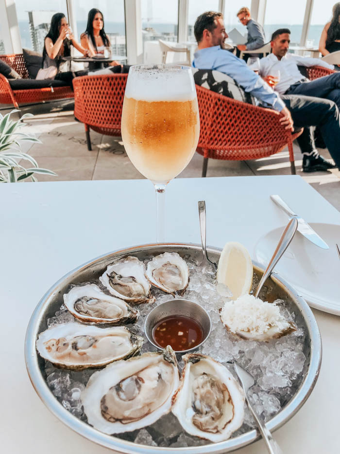 A restaurant patio full of happy diners has a bowl of oysters on ice prominently displayed, accompanied by a beer Oysters and beer on a restaurant patio