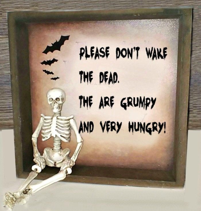 Small skeleton sitting on a wooden tray decorated with bats and a message that reads "please don't wake the dead. They are grumpy and very hungry." Halloween tray with a spooky message