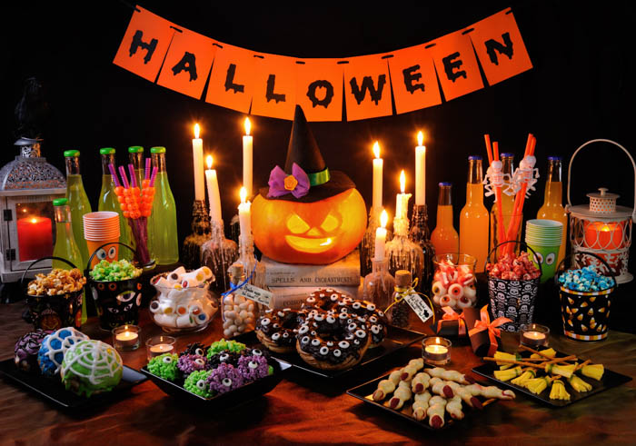 A Halloween buffet table with food, drinks, candles, a pumpkin and a banner that says "Halloween". A Halloween buffet table with food, drinks, candles, a pumpkin and a banner that says "Halloween".