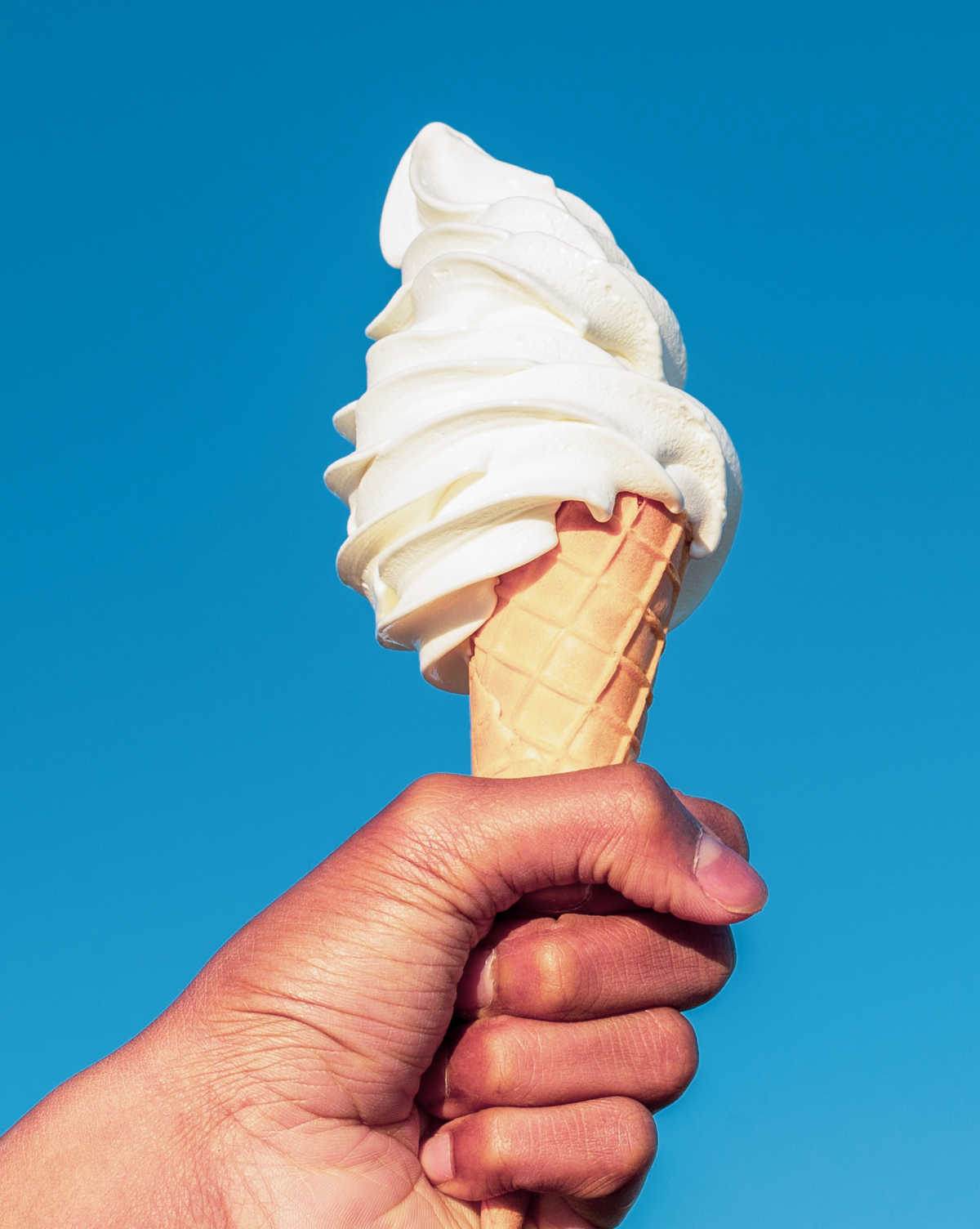 Celebrate National Ice Cream Cone Day! Hand holding a vanilla ice cream cone.