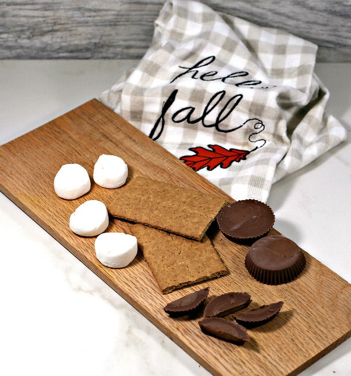 Cutting ingredients for cookies. Cut peanut butter cups and marshmallows with graham crackers on a board.