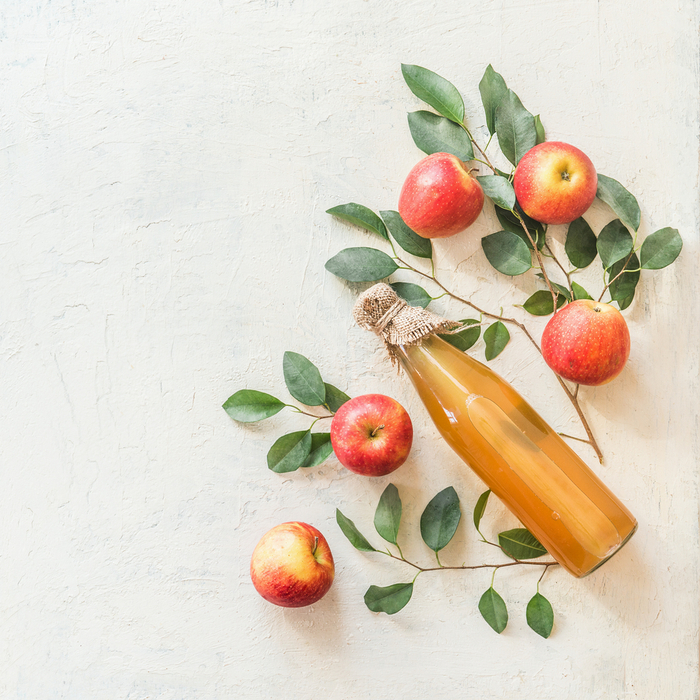 A bottle of apple cider next to apples. A bottle of apple cider surrounded by apples and apple branches.