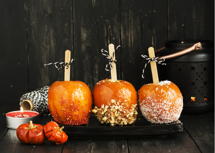Three caramel apple with different toppings against a wooden backdrop. Three caramel apple with different toppings (nuts, sprinkles and coconut) on a slate board against a dark wood background.