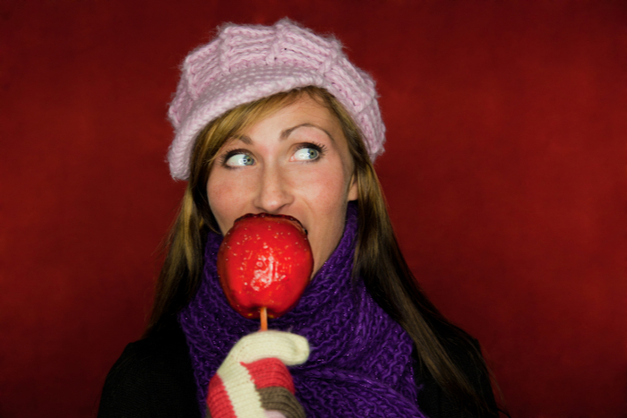 Woman eating a candy apple. A woman dressed seasonally for winter, eating a candy apple.