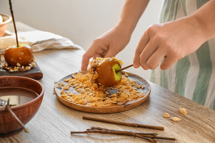 A person coating a caramel apple with cornflakes. A person coating a caramel apple with cornflakes paying homage to the man who invented caramel apples.