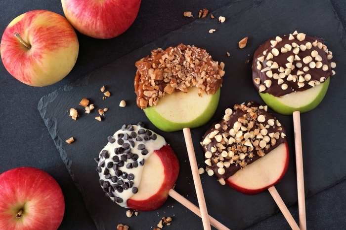 Two caramel apples for halloween with sprinkles. Caramel apple slices on sticks with chocolate chip toppings.