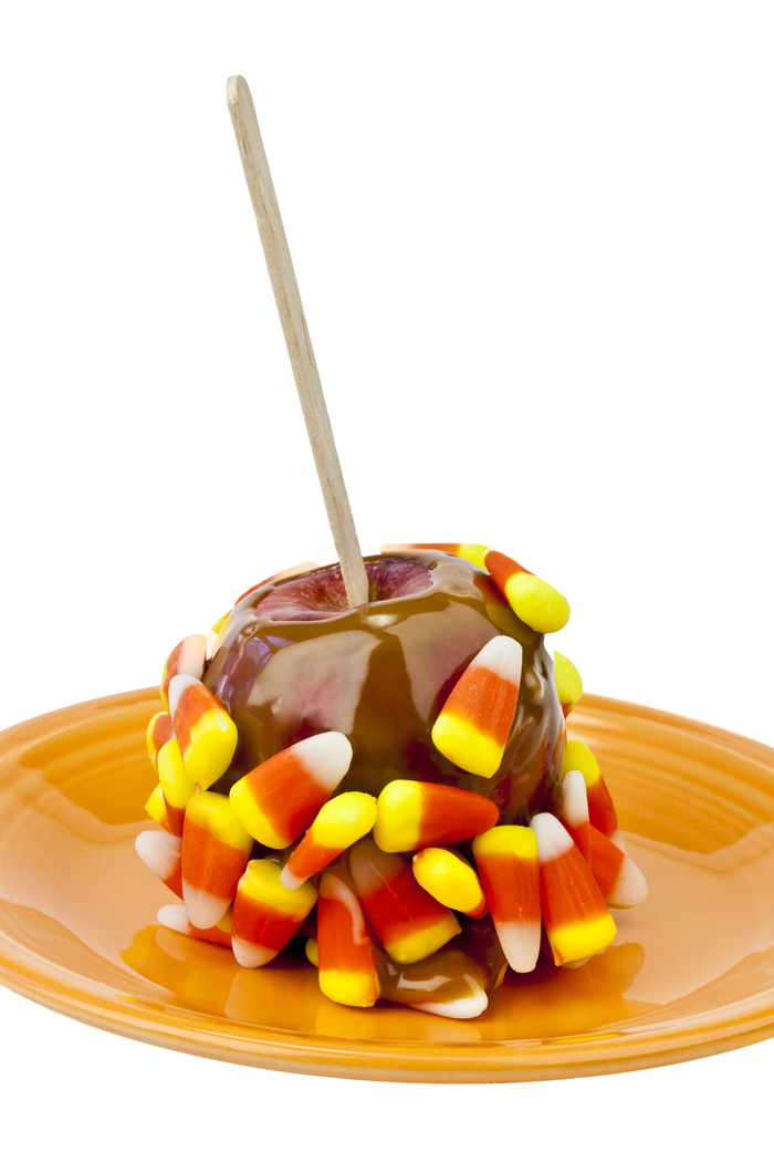 A candy corn caramel apple. A candy corn caramel apple sitting on a plate against a white background.