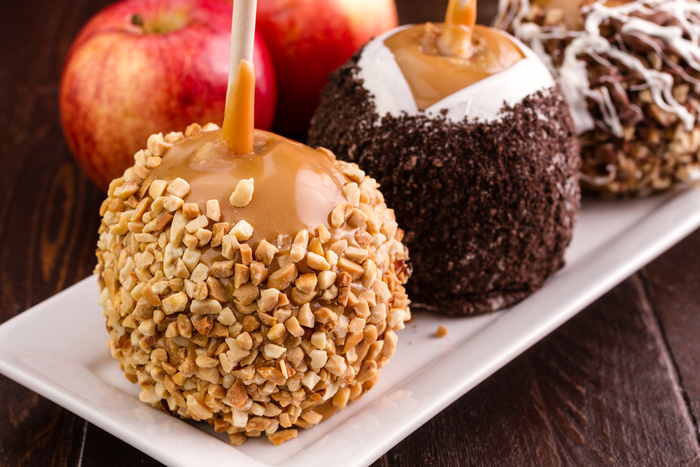 A plate with three caramel apples, each with a different topping. A variety of caramel apples on a plate with different toppings including peanuts, Oreos and white chocolate.