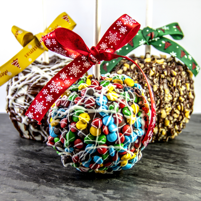 Three caramel apples with different candy on them including m&ms. Three caramel apple toppings with bows tied on the sticks and different candy on them including m&ms.