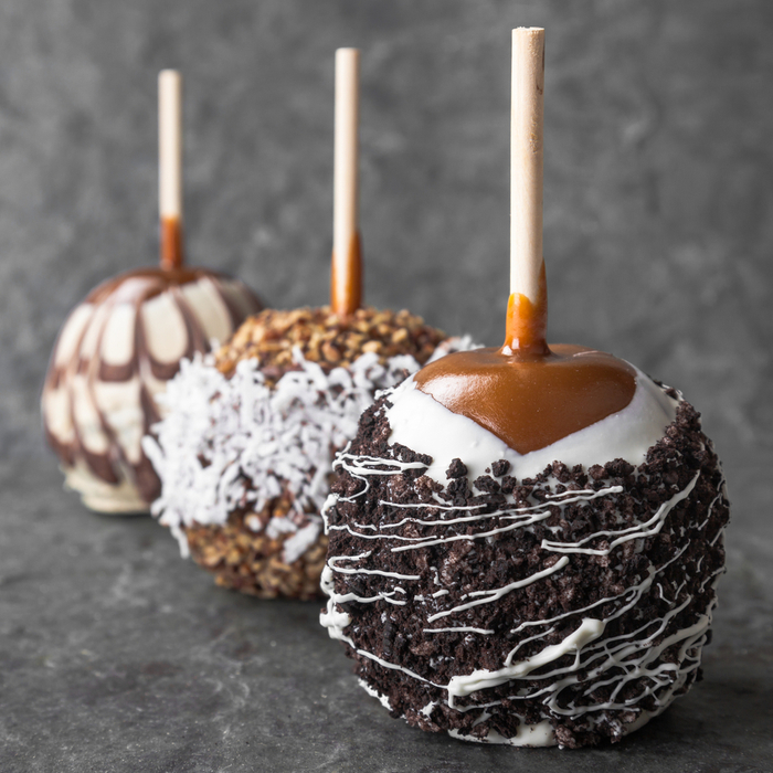 Three caramel apples with different toppings such as oreo crumbles, white chocolate, coconut, milk chocolate and nuts.