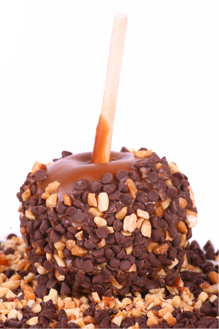 A caramel apple with mini chocolate chips and peanuts. Caramel apples with chocolate chips and peanuts on top of a pile of chocolate chips and peanuts.