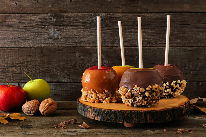 Caramel apples with peanuts and chocolate caramel apples with peanuts as toppings on a wooden display platter. A wooden display platter holding caramel apples and chocolate caramel apples with peanut toppings and chocolate toppings.