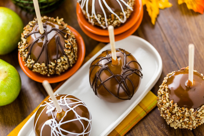 An assortment of caramel apples with white and dark chocolate. An assortment of dark chocolate caramel apples and white chocolate caramel apples, some with peanuts.