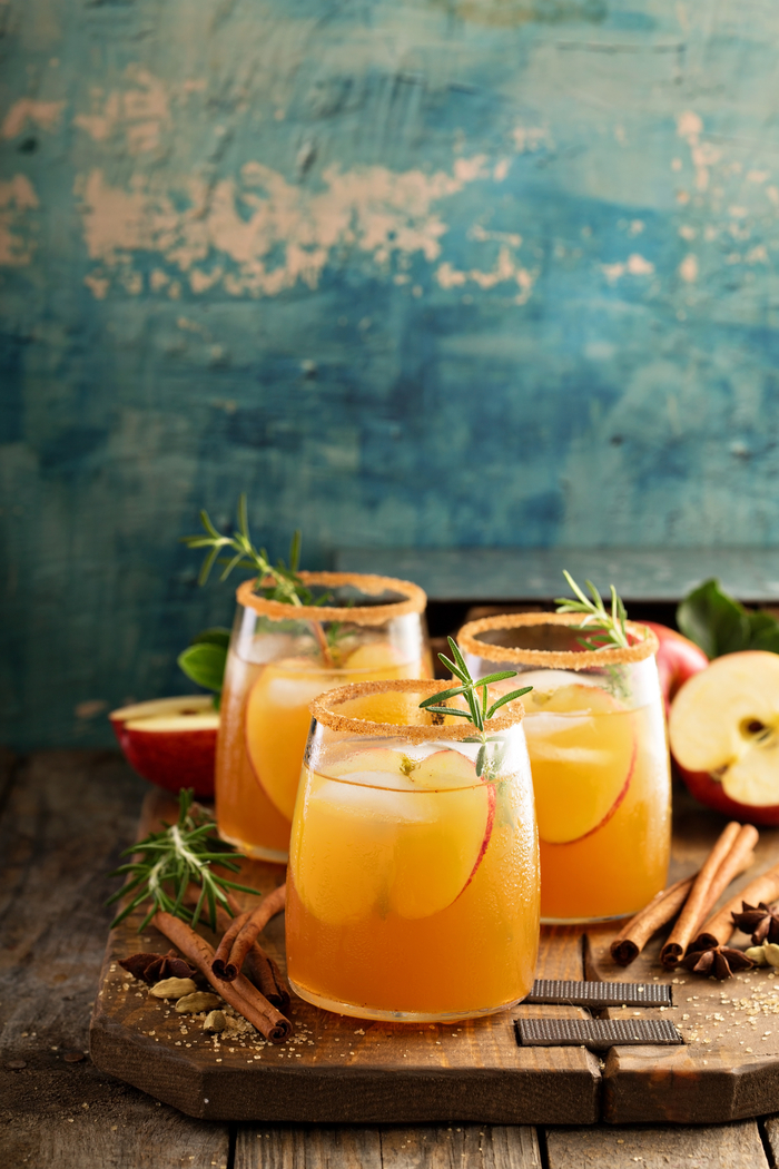 Three apple cider cocktails. Three apple cider cocktails with apples and rosemary garnishes for apple cider day.