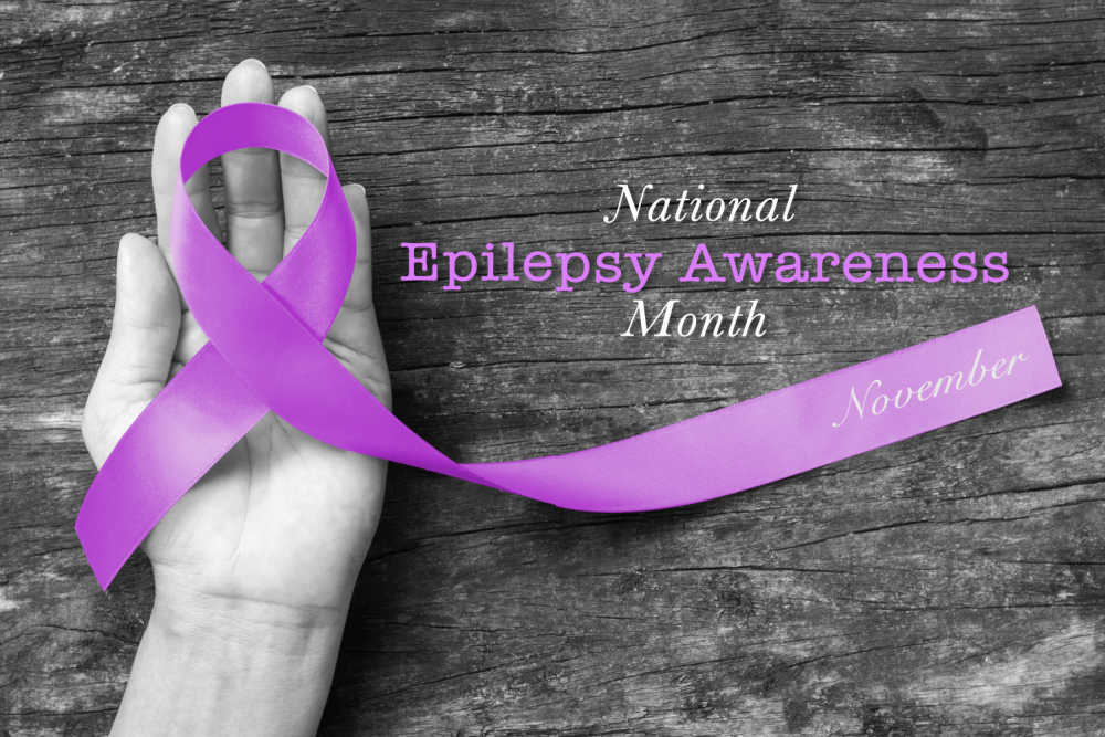 National Epilepsy Awareness Month - November. Hands holding a purple ribbon and words National Epilepsy Awareness Month - November.