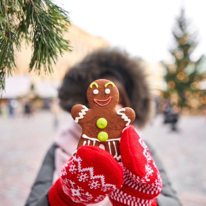 A woman holding up a gingerbread cookie in front of her face at a Christmas market.