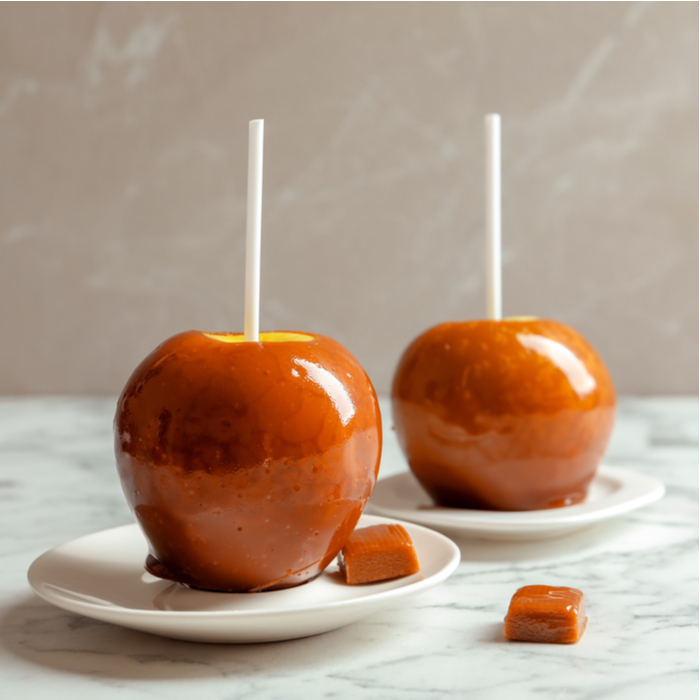Two caramel apples on plates with caramels next to them. Two caramel apples on plates with caramel candy beside them.