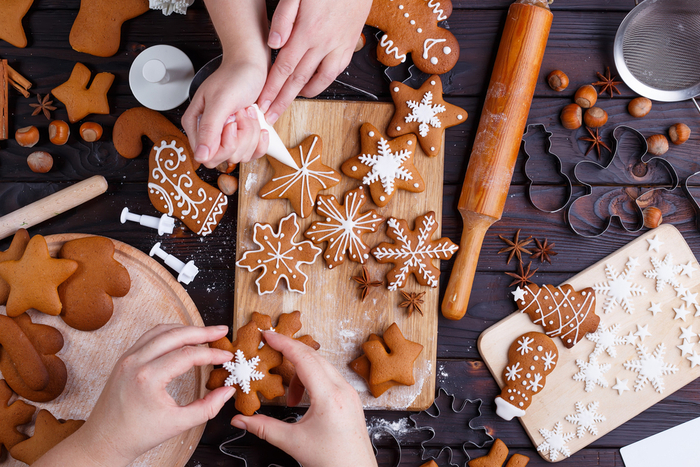 A counter with gingerbread cookies and icing supplies and two sets of hands decorating the cookies.