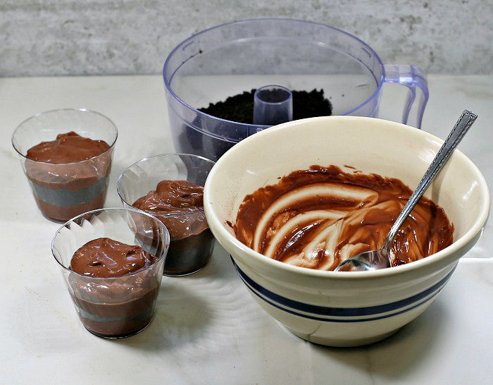 Layering the pudding cups. Cups of pudding with an empty pudding bowl and food processor bowl of cookie crumbs.