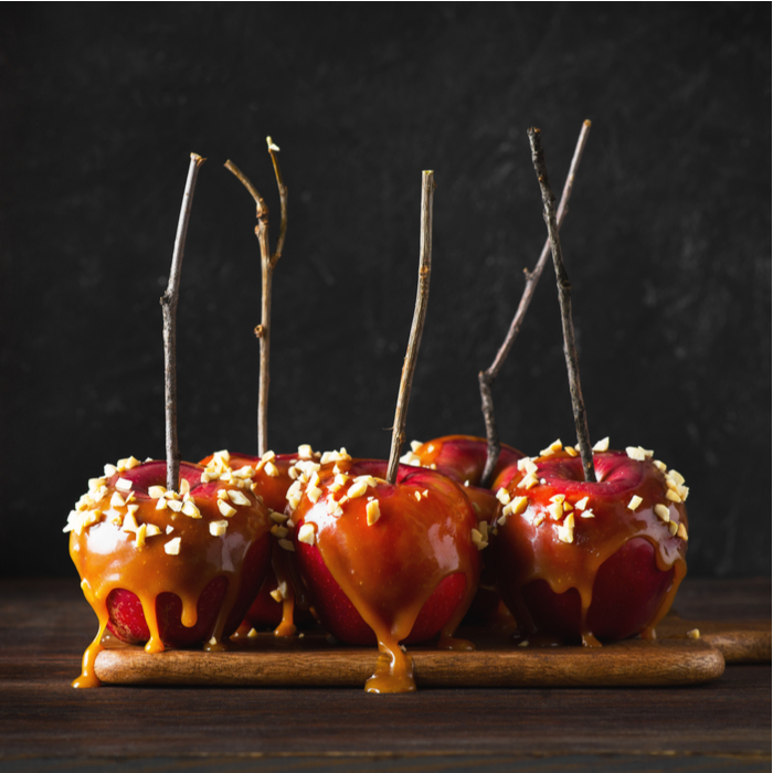 Rustic caramel apple with twigs for sticks and peanut toppings. A plate of rustic caramel apple with twigs for sticks and peanut toppings.