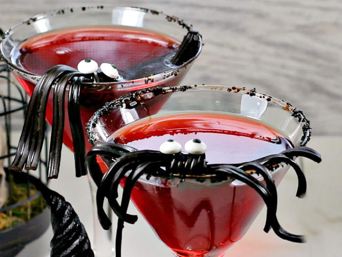 Vampire cocktail with black licorice spider Two spider garnishes sitting in a two martini glasses filled with red Halloween cocktails with black rim.