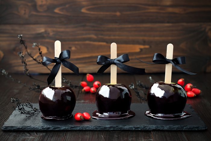 Three black caramel apples with bows. Three black spooky caramel apples with bows on a slate serving platter.