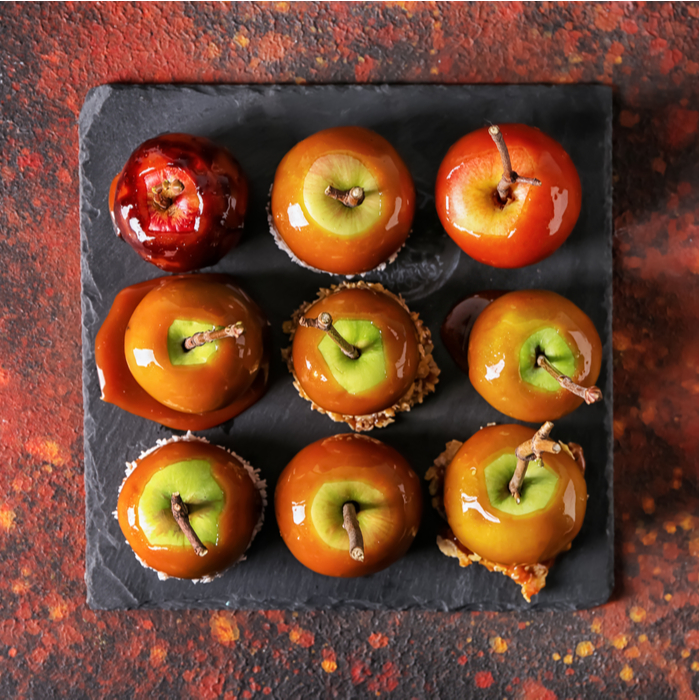 Nine caramel apples on a slate serving tray. Nine unique caramel apples on a slate serving plate on an abstractly marbled background of fall colors.