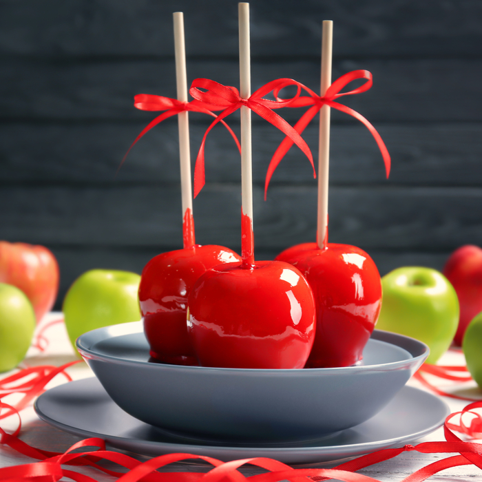Three candy apples for Christmas with bows on them, on a plate.