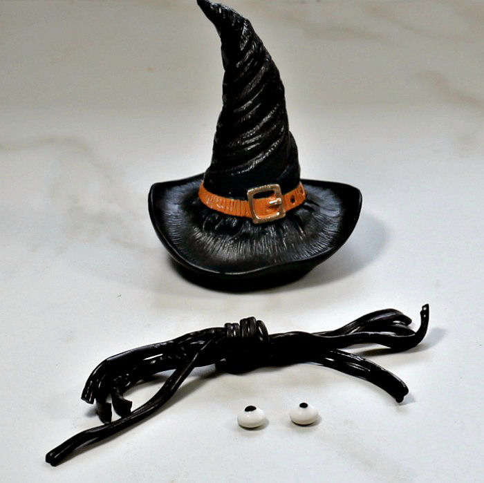 Making a licorice spider garnish A progress shot of making a licorice spider Halloween garnish, positioned in front of a decoration shaped like a witches hat.