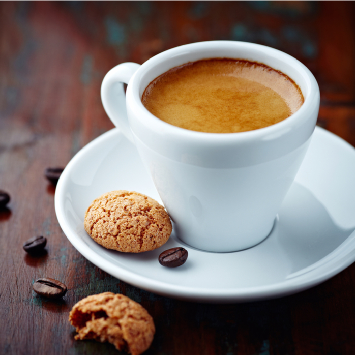 A shot of espresso with a small biscotti beside it on a saucer.