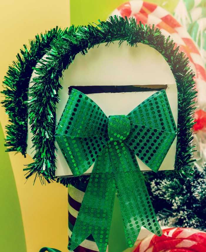 Mailbox decorated with green garland and bow. White mailbox with green garland and metallic bow.