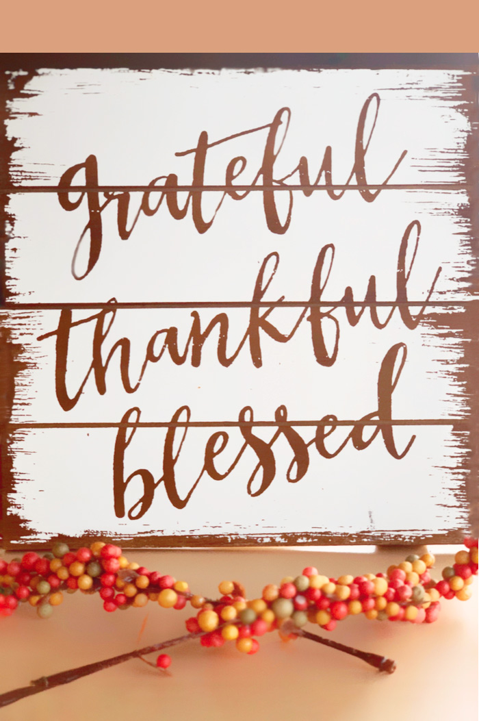 A wooden decor board with the Thanksgiving quote "Grateful, thankful, blessed" painted on it.