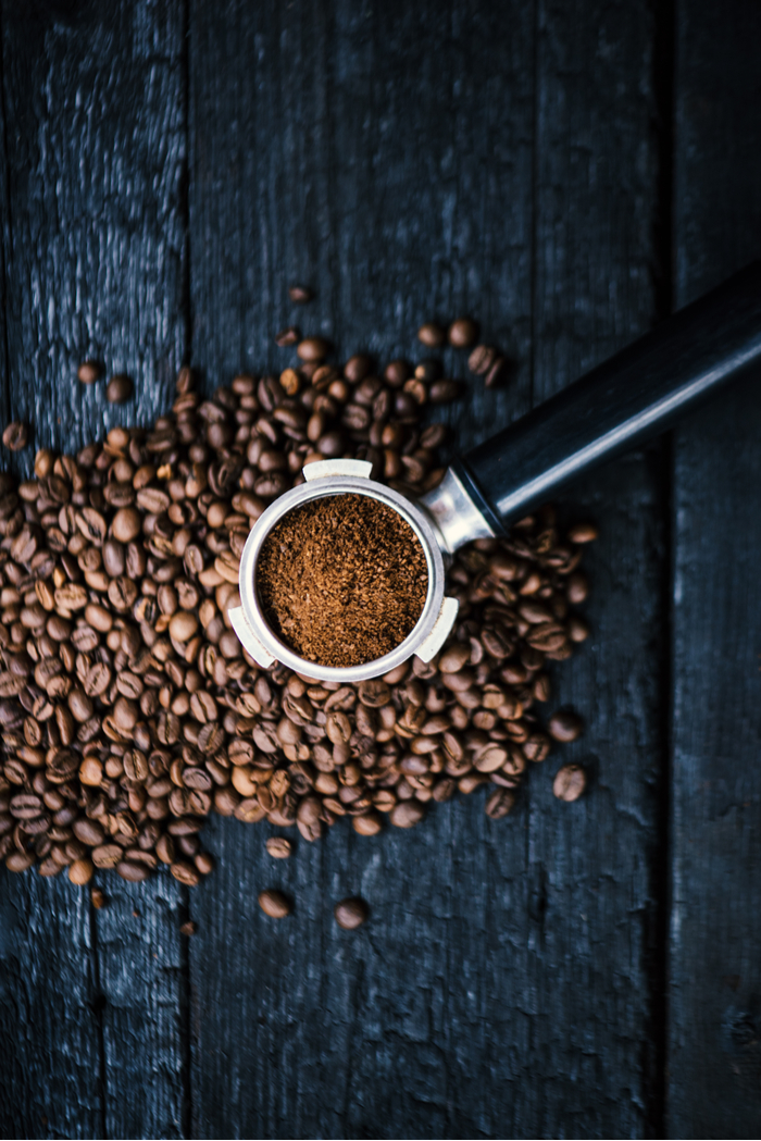 A portafilter over coffee beans. A portafilter filled with espresso grounds over coffee beans on a dark wooden background.