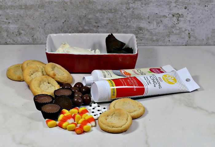 Frosting tubes and piles of frosting with sugar cookies, malted milk balls, peanut butter cups, candy corn and edible eyes - ingredients for Thanksgiving turkey cookies.