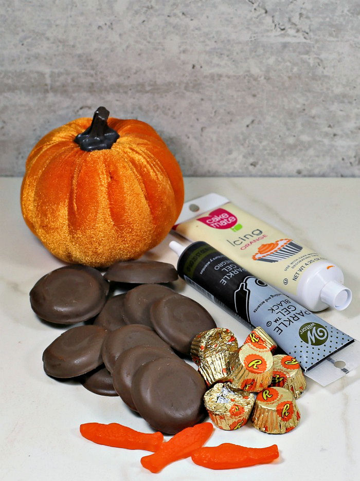 Ingredients for pilgrims hats Chocolate cookies, peanut butter cups, Swedish fish, frosting tubes and velvet turkey on a counter.