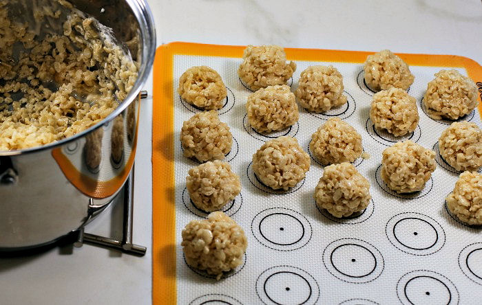Making Rice Krispie balls. Balls of Rice Krispie treat mixture on a silicone mat near a bowl of Rice Krispie cereal and marshmallows..