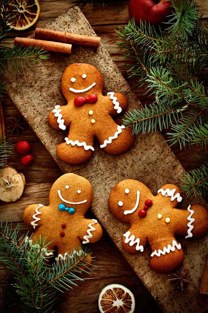 Gingerbread men Three gingerbread cookies arranged on a table with fir branches and cinnamon sticks.
