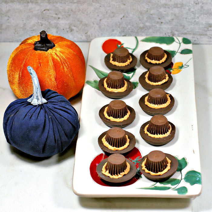 Pilgrim hat cookies on a plate. Pilgrim hat cookies on a plate with orange hat brims made of frosting and two velvet pumpkins.