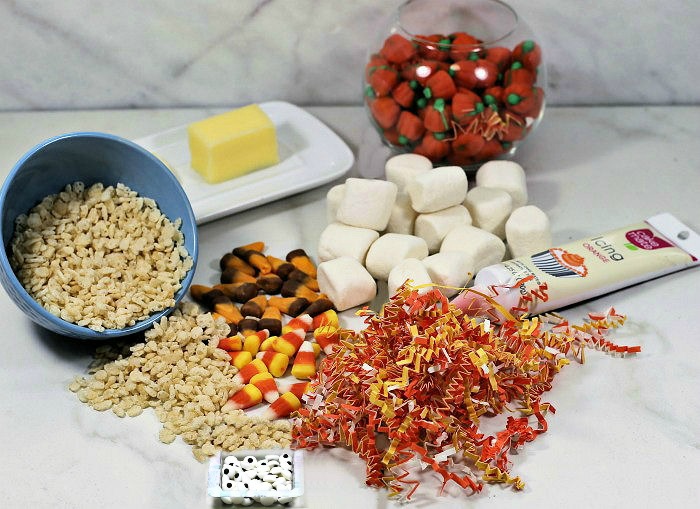 Supplies for turkey pops. Rice Krispies, marshmallows, butter, candy, bowl, sticks, frosting, crinkled paper, and edible eyes.
