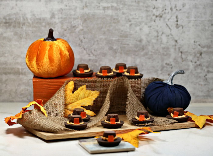 Display of pilgrim hat cookies with pumpkins, burlap and leaves.