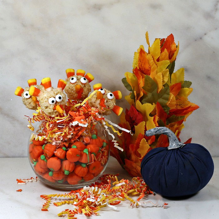 Rice Krispie turkey pops in a bowl of candy pumpkins and paper with a leaf tree and blue velvet pumpkin.