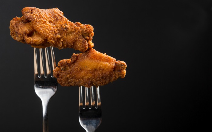 Chicken wings and flats. Two forks holding breaded, fried chicken wings and flats.