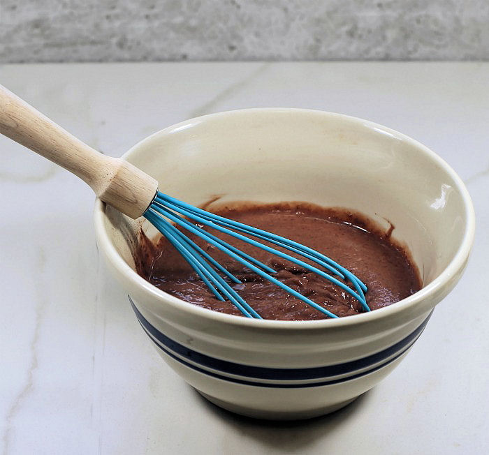 Making chocolate pudding chocolate pudding in a striped bowl with a blue whisk.